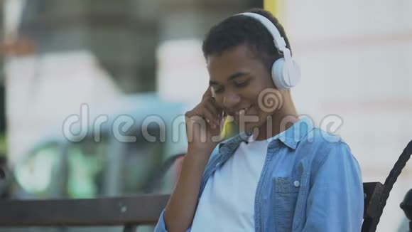 积极的年轻人用耳机听音乐坐在长凳上跳舞视频的预览图