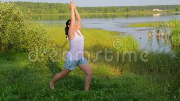 布鲁内特女士早上在湖上做英雄式的瑜伽视频的预览图