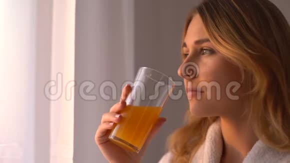 穿长袍的女孩喝橙汁看窗户皮肤维生素面部护理视频的预览图