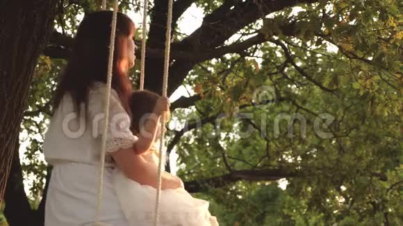 快乐的妈妈把一个快乐的女儿卷在橡树上的公园里的秋千上幸福家庭的概念单身母亲视频的预览图