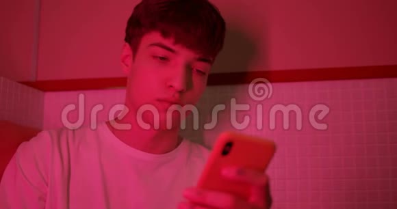 穿着白色T恤的年轻时尚男士用智能手机坐在未来的霓虹灯蓝色视频的预览图