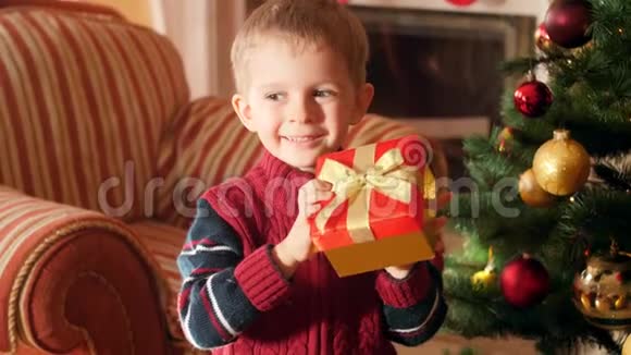 4k视频快乐的笑着小男孩带着圣诞礼物站在漂亮的盒子里看圣诞树视频的预览图