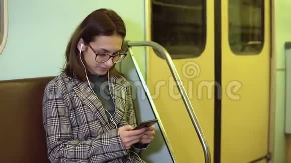 一个年轻的女人用耳机听音乐她手里拿着一部手机在地铁火车上这个女孩正在写信视频的预览图