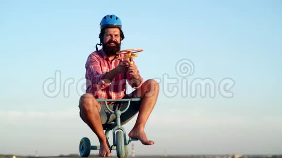 长胡子的滑稽男人在天空背景下骑着儿童自行车玩得很开心一个长胡子的滑稽男人骑着儿童自行车视频的预览图