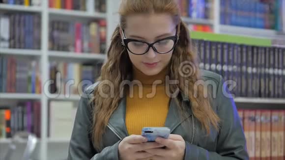 年轻漂亮的女人戴着眼镜微笑的年轻女孩的肖像女孩在城市大学图书馆打电话视频的预览图