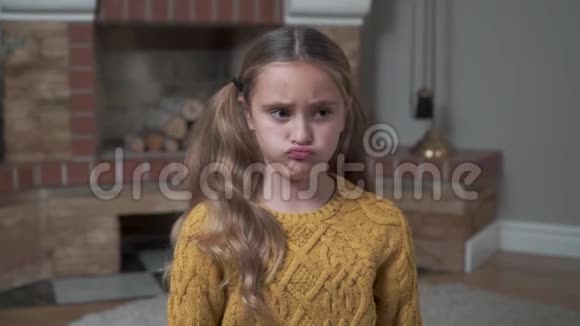 一个穿着芥末毛衣的沮丧的白人女孩坐在家里壁炉前的肖像伤心的孩子视频的预览图