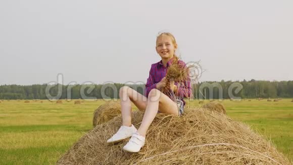 无忧无虑的青少年女孩在农村撒干稻草快乐少女坐在干草堆上少女视频的预览图