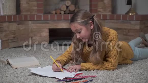 一个可爱的白人女孩的肖像长马尾辫躺在柔软的地毯上画画可爱的孩子在休息视频的预览图