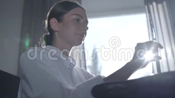专业女医生看着喷药注射器坐在桌子旁背景是一个视频的预览图