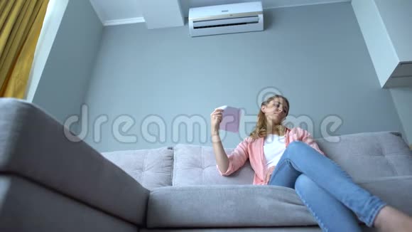 坐在沙发上挥舞着纸的女人浑身发热空调故障视频的预览图
