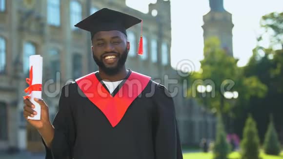 兴奋的美国黑人学生穿着毕业礼服拿着文凭看相机视频的预览图