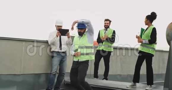 有魅力的工程师留着胡子在休息时间在建筑屋顶的同事面前跳舞视频的预览图