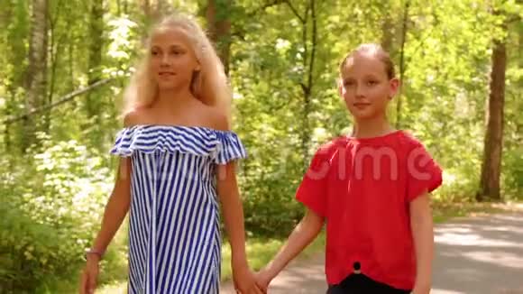 微笑的女朋友牵着手在夏季公园散步阳光明媚的一天两个快乐的女孩在城市的小路上散步视频的预览图