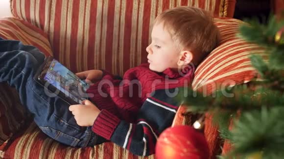 4k小男孩躺在客厅扶手椅上在数码平板电脑上玩电子游戏的特写视频视频的预览图