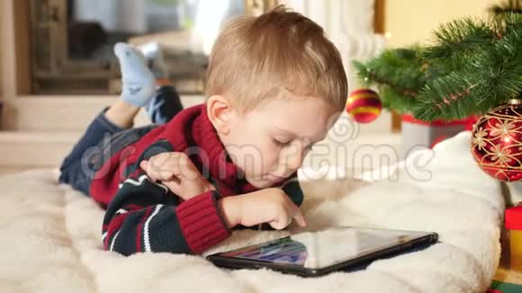 小男孩在家中躺在圣诞节树旁边时使用和玩数字计算机的4k视频儿童视频的预览图