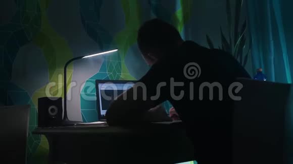 他坐在桌子前写字在笔记本电脑前晚上晚上公寓台灯视频的预览图
