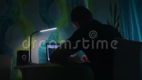 他坐在桌子前写字在笔记本电脑前晚上晚上公寓台灯视频的预览图