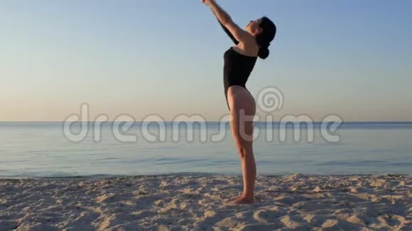 运动的女人穿着黑色紧身衣在令人惊叹的日出时在海边做瑜伽健身运动瑜伽和健康生活方式视频的预览图