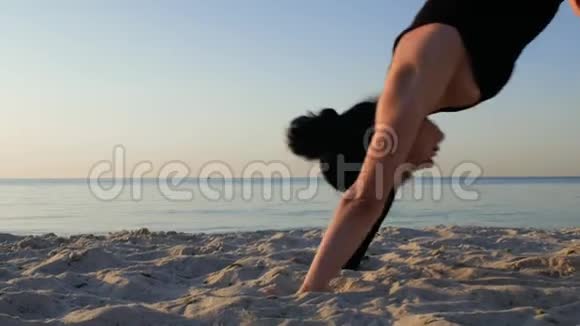 太阳升起时穿黑色紧身衣的运动黑发女人在海边做瑜伽健身运动瑜伽和健康的生活方式概念4k视频的预览图