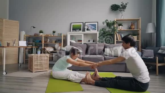 女孩和男人做瑜伽伸展手臂腿回到家坐在垫子上视频的预览图