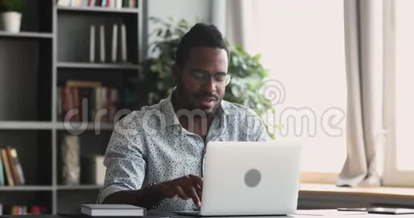专注于在家里办公室的笔记本电脑上打字的非洲男人视频的预览图