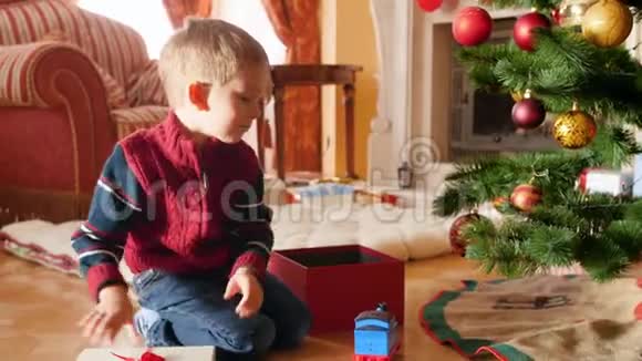 小男孩在圣诞树下的漂亮礼品盒中包装玩具的4k视频儿童赠送礼物和礼物视频的预览图
