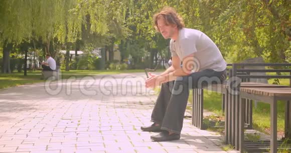 可爱的白种人坐在户外公园里的长椅上视频的预览图