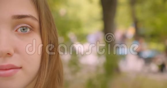 年轻可爱的白种人女性特写半张脸的肖像看着镜头开心地站在户外公园里视频的预览图