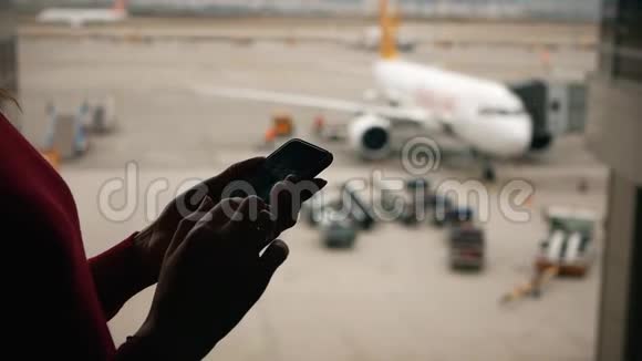 女的手拿着一部智能手机放在机场候机楼窗外的客机背景上视频的预览图