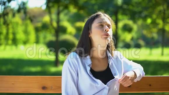 年轻女子在公园的长凳上休息患有高温和闷热患有PMS视频的预览图