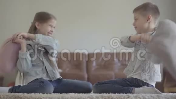 可爱的双胞胎女孩和男孩友好地在客厅里打架枕头穿着同样的衣服笑着视频的预览图