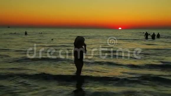 日落时分一个戴着帽子的女人沿着海滨散步剪影视频的预览图
