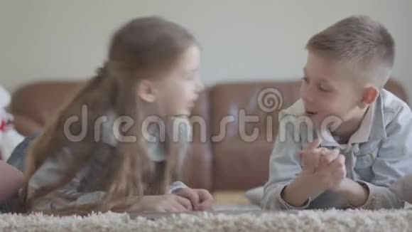 可爱的双胞胎男孩和女孩躺在地毯上谈论着一些有趣的游戏笑着笑着视频的预览图