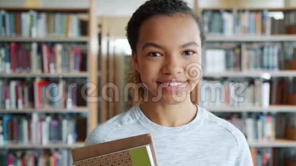 富有魅力的非裔美国学生在图书馆捧着书微笑的画像视频的预览图