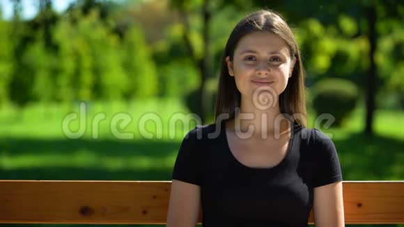 快乐的年轻女子坐在公园的长凳上微笑着休闲活动户外视频的预览图