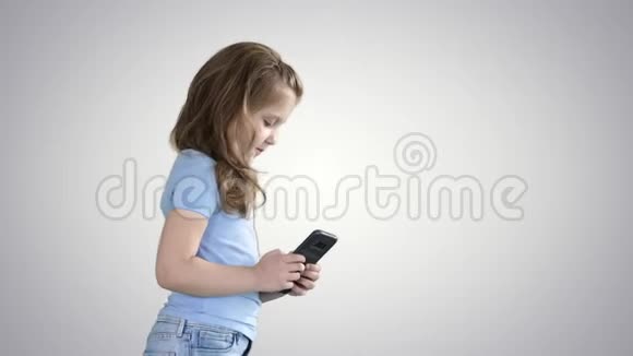 小女孩在梯度背景下行走时玩智能手机视频的预览图