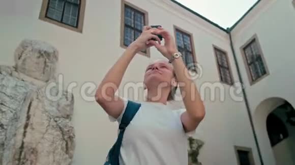 穿着白色T恤的旅游女孩通过电话在城堡里观看全景照片视频的预览图