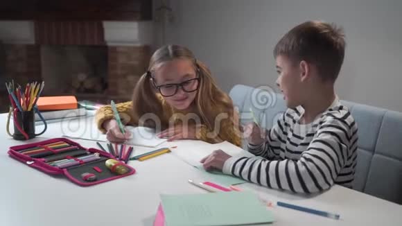 两个快乐的高加索儿童微笑着在练习本中写作穿条纹夹克的男孩和戴眼镜的女孩视频的预览图