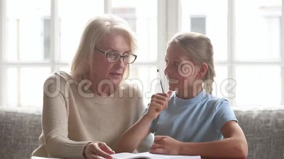 年长家庭教师或祖母帮助孩子或孙女做家庭作业视频的预览图