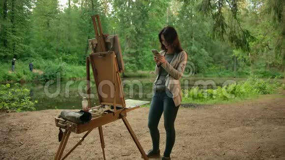 一位女孩艺术家旁边是画架和调色板在社交网络上与她的朋友交流视频的预览图