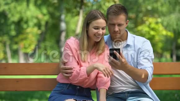 快乐的一对情侣一起在公园里看智能手机上的照片约会视频的预览图