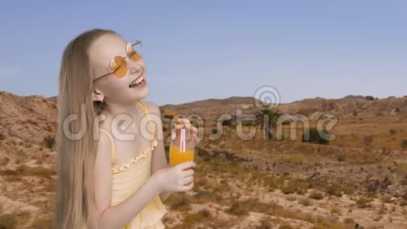 兴奋的女孩带着橙汁杯在沙漠和山的背景上笑捧着橘子笑的少女视频的预览图