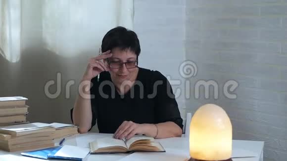 女人翻阅一本悠闲的书坐在昏暗的灯光背景下的白色桌子旁视频的预览图