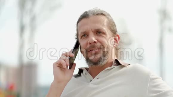 轻松迷人的中年男人长发在智能手机上说话笑和微笑视频的预览图