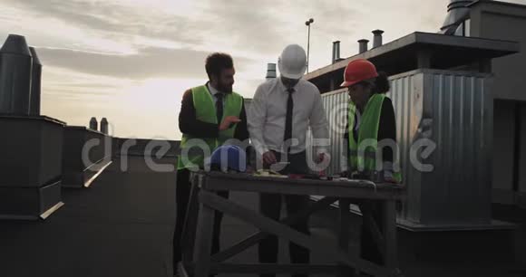 三个建筑工人围着一张桌子看着建筑的蓝图他们都指向董事会视频的预览图