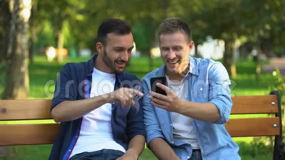最好的男性朋友在智能手机上看照片在公园玩得开心视频的预览图