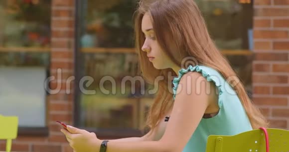 年轻有魅力的白种人女性使用手机坐在户外咖啡馆的特写镜头视频的预览图