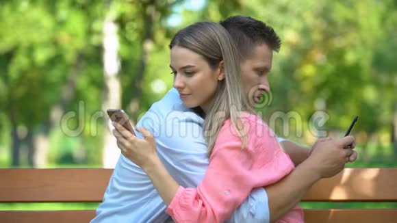 年轻夫妇在公园拥抱在智能手机上聊天缺乏沟通视频的预览图