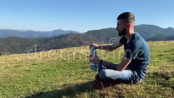 一个年轻人从热水瓶里喝茶看着山视频的预览图