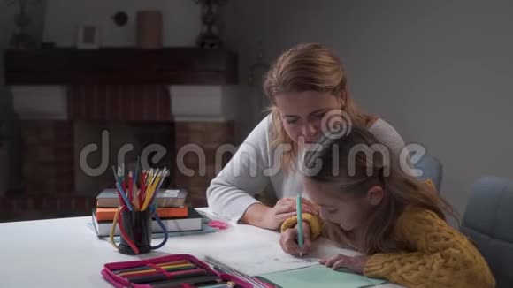 年轻的高加索母亲和她可爱的女儿做家庭作业小聪明的女孩写作业本妈妈视频的预览图